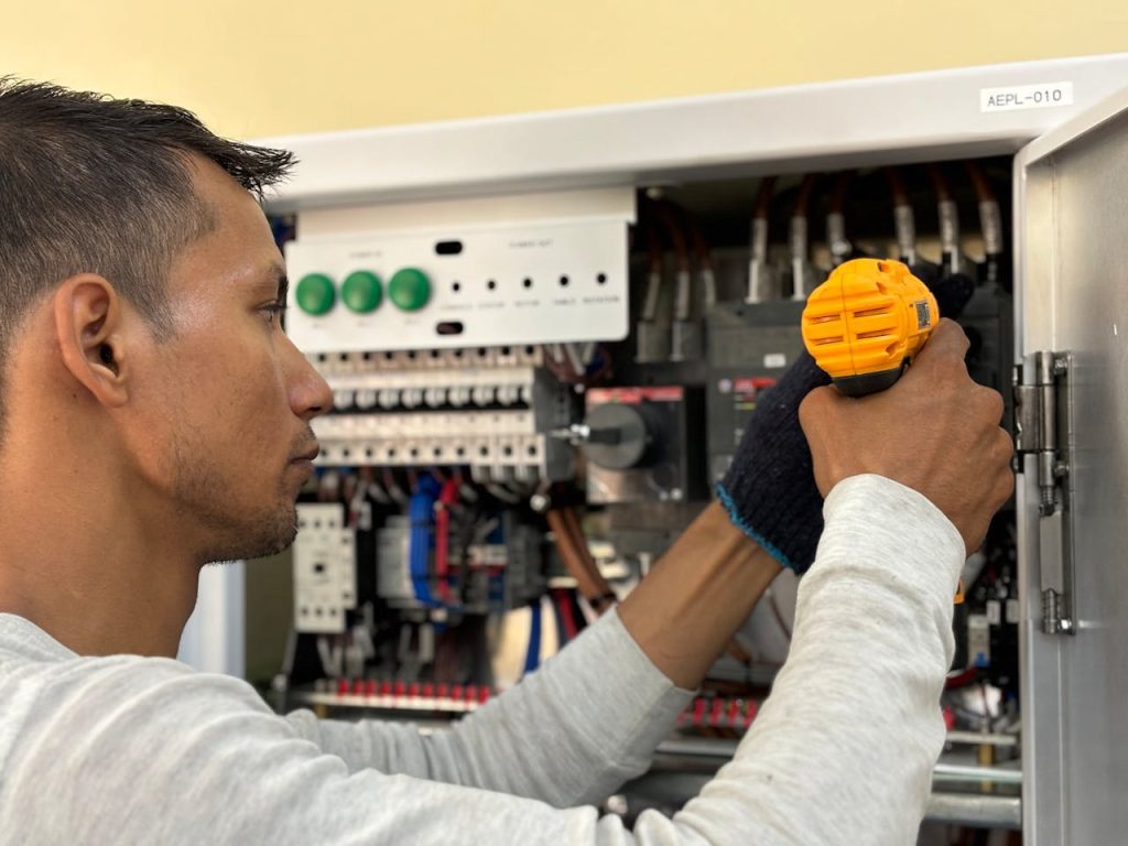 NR Electric Job 2 Skilled electrician using a drill to repair electrical equipment indoors. Focus on precision and safety.